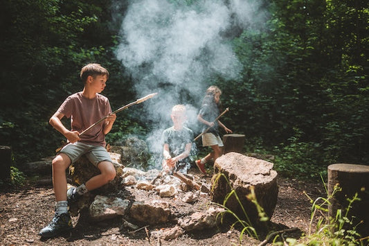 Trois enfants sont dans la forêt en train de griller du pain au serpent sur un feu.