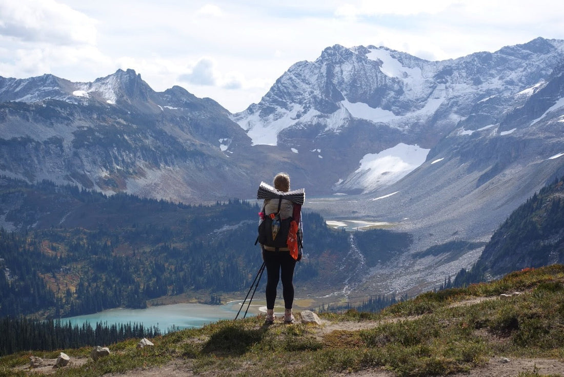 Long-distance hiker with rucksack on a thru-hike in the mountains - view over a wide, untouched landscape with lake and snow in the distance.