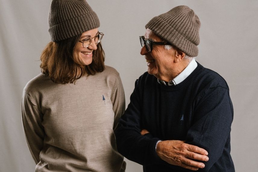 A woman and a man look at each other laughing and wearing knitted dresses.