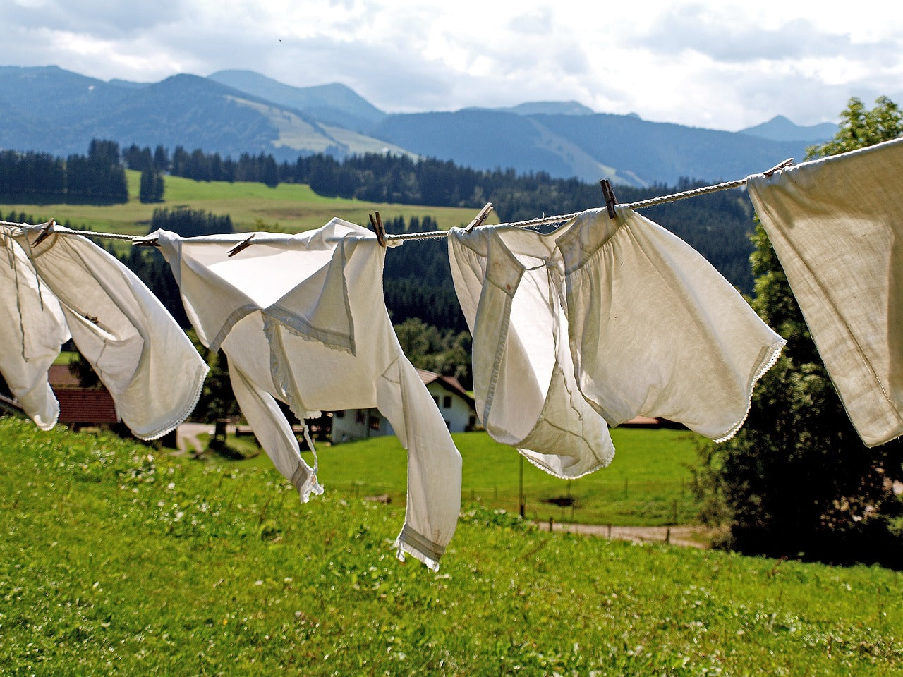 Du linge blanc sur une corde à linge dans le vent, avec des prairies vertes, des fermes et des montagnes en arrière-plan - un séchage durable en pleine nature.