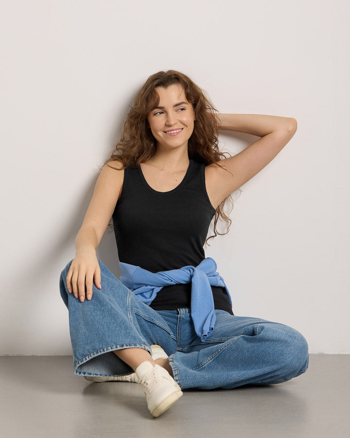 NIKIN  women in black, with long sleeves, paired with jeans; the model is sitting on the ground and smiling.